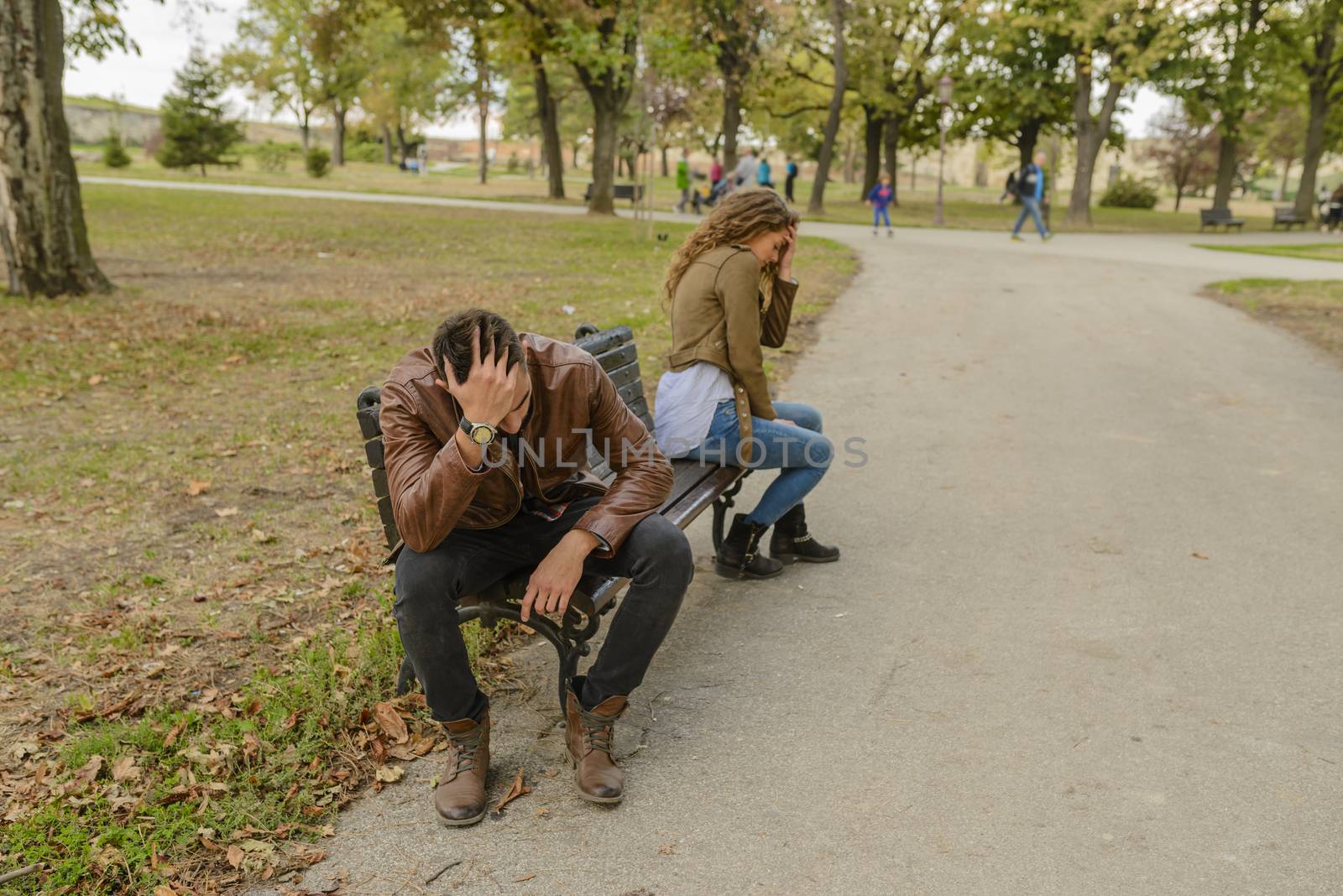 Attractive and modern lovers feeling disappointed after breaking up long relationship. Sitting on the bench in public park.