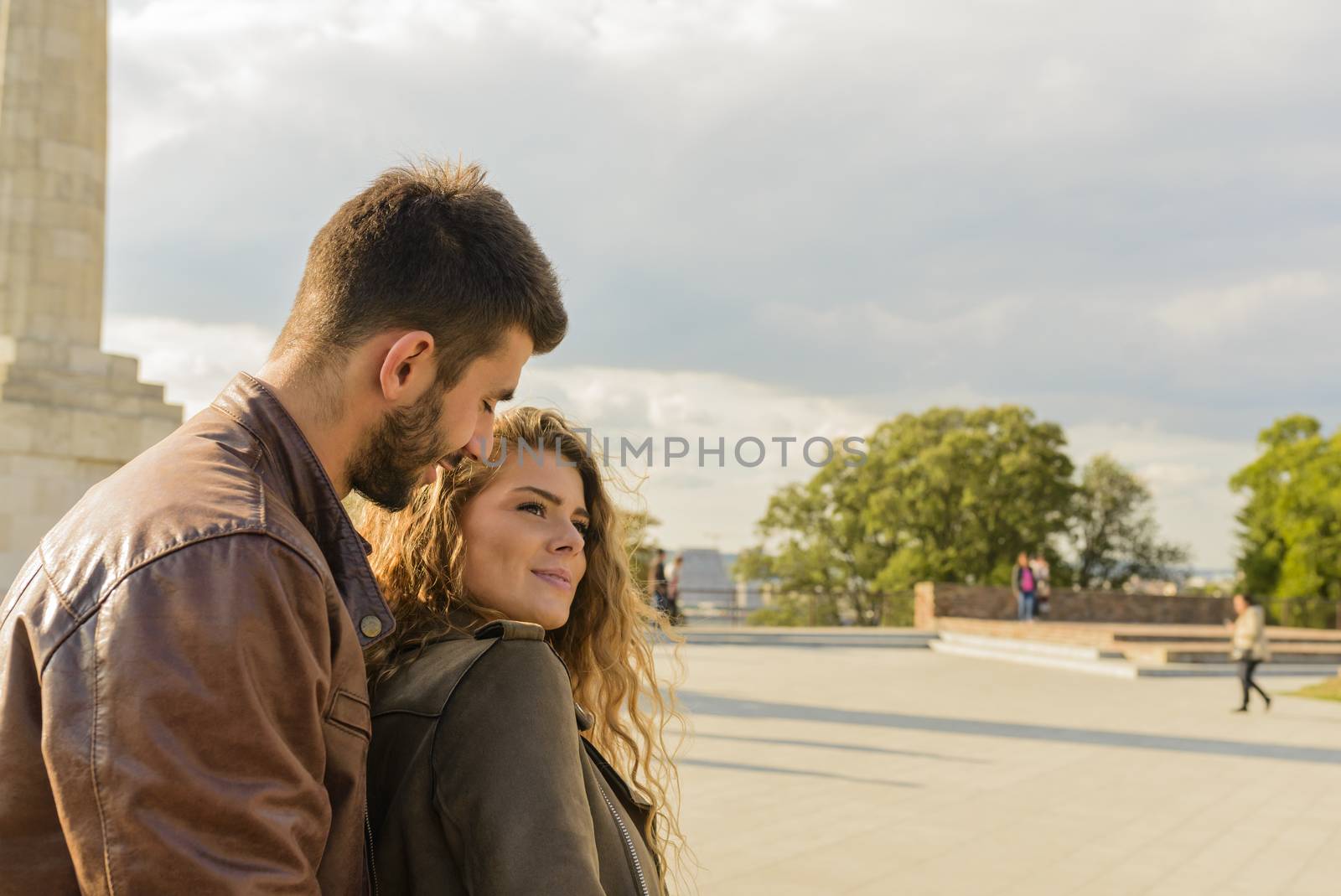 Good-looking young man is holding his attractive girlfriend from the back while walking and smiling