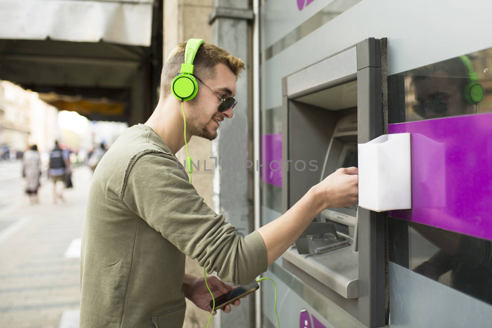 Young handsome man with sunglasses and headphones taking money from the ATM