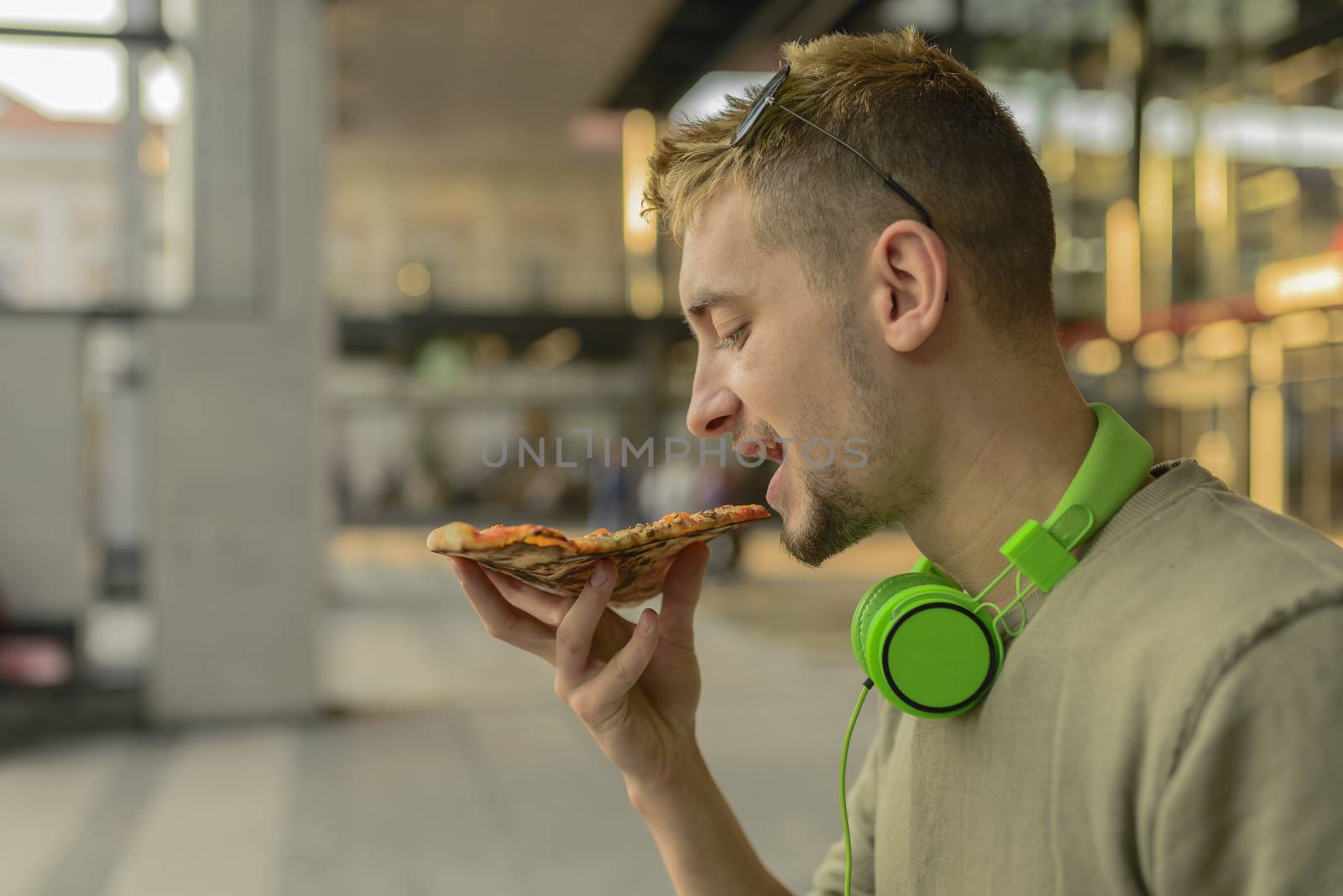 Handsome young man with headphones eating pizza in the city street