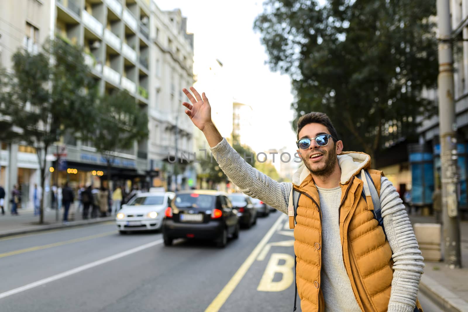 Handsome hipster with orange jacket and sunglasses stopping taxi in the city street