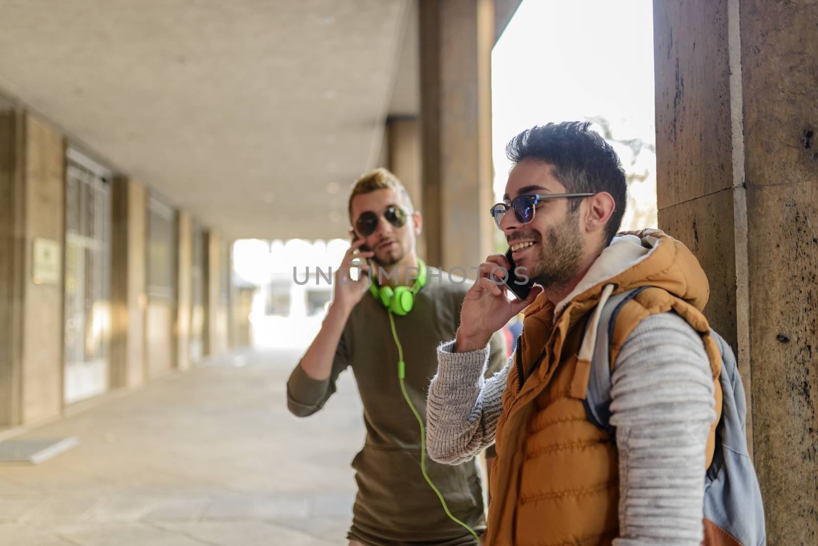 Two young men talking on the phone in city passage