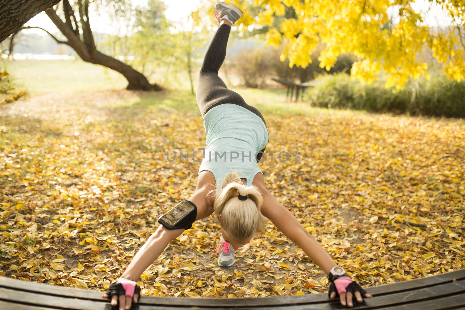 Young sportswoman stretching her legs at wooden bench in public park