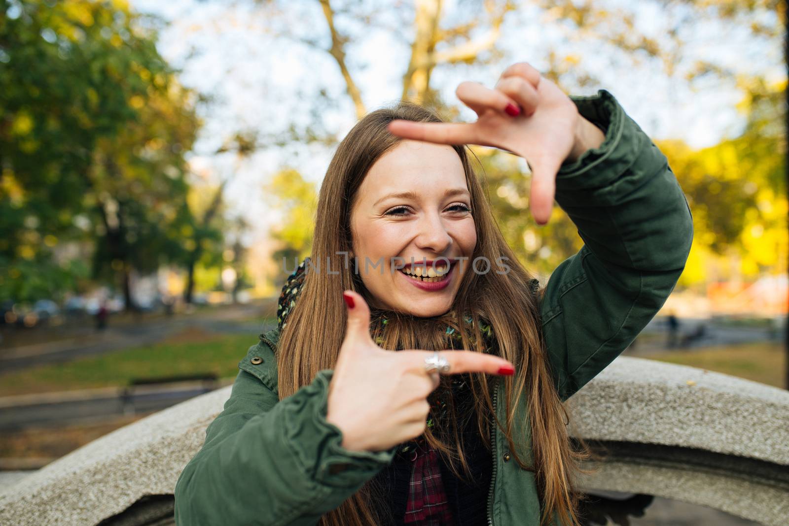 Attractive young woman in green coat making finger frame outdoors