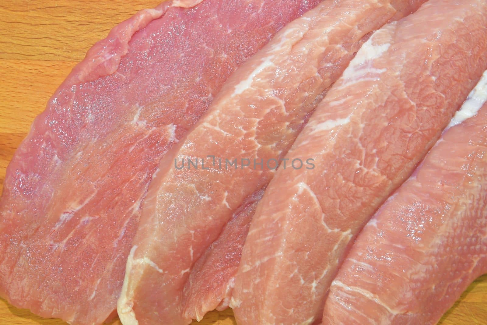 Raw pork loin chops on a cutting board on brown cutting board. Slices of pork steaks. Pork chops ready to fry. Selective focus.