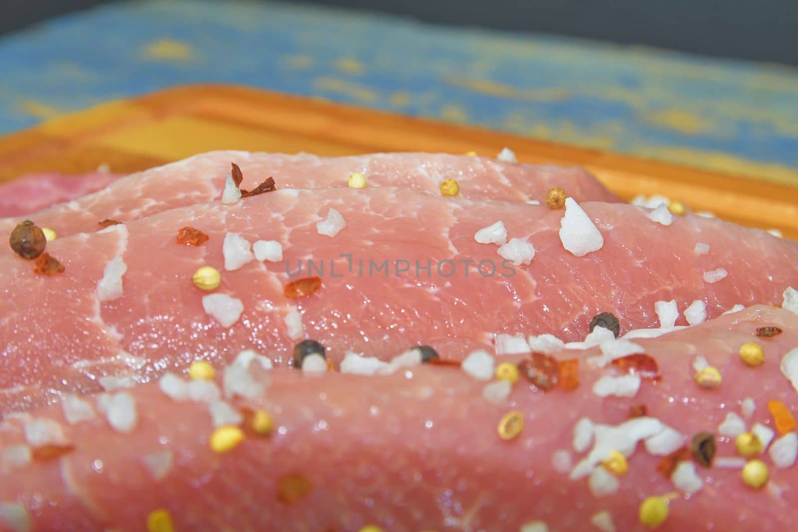 Raw pork loin chops on a cutting board with salt, pepper on brown cutting board. Slices of pork steaks. Pork chops ready to fry. Selective focus by roman_nerud