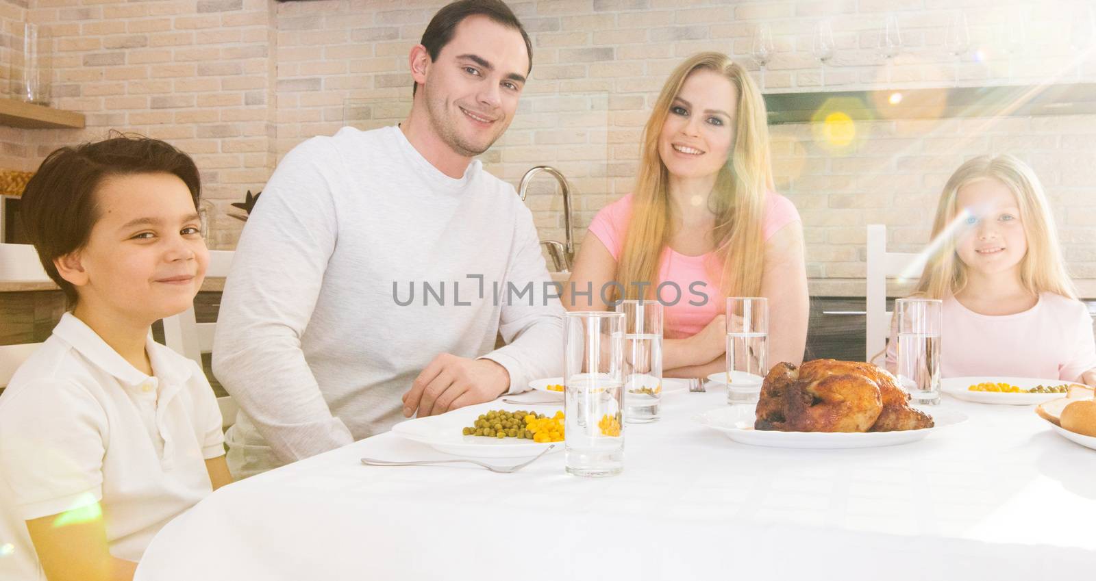 Happy family of parents and children having roast chicken dinner at table