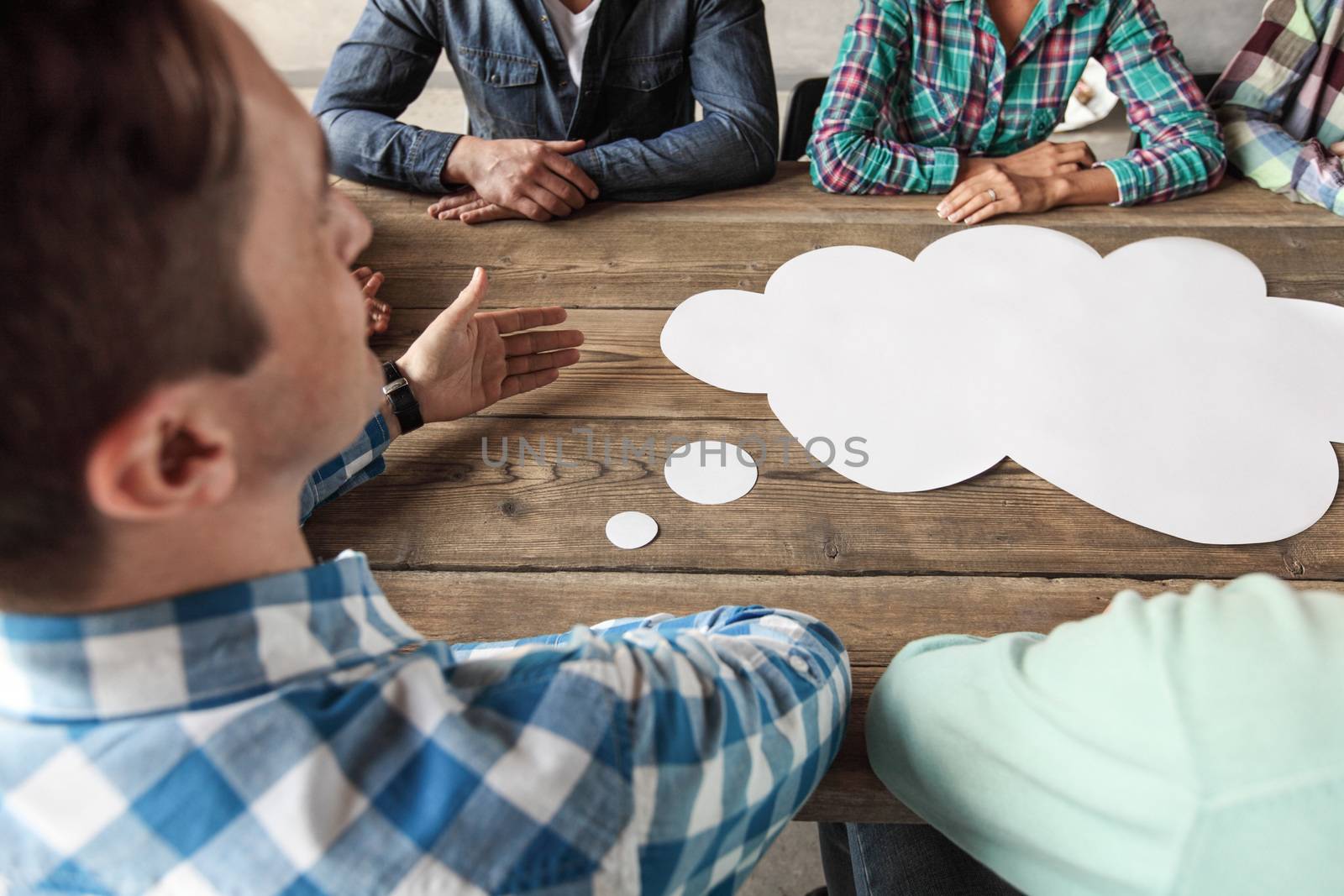 Hipster business teamwork brainstorming planning meeting concept, man tells his opinion, people sitting around the table with white paper shaped like dialog cloud