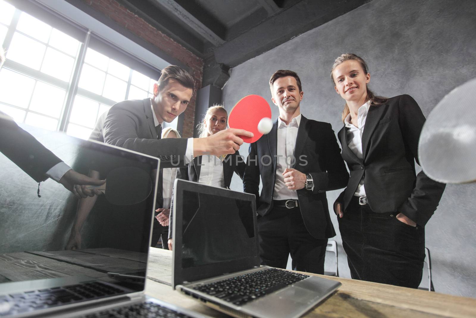Business people play ping pong on office table with laptops