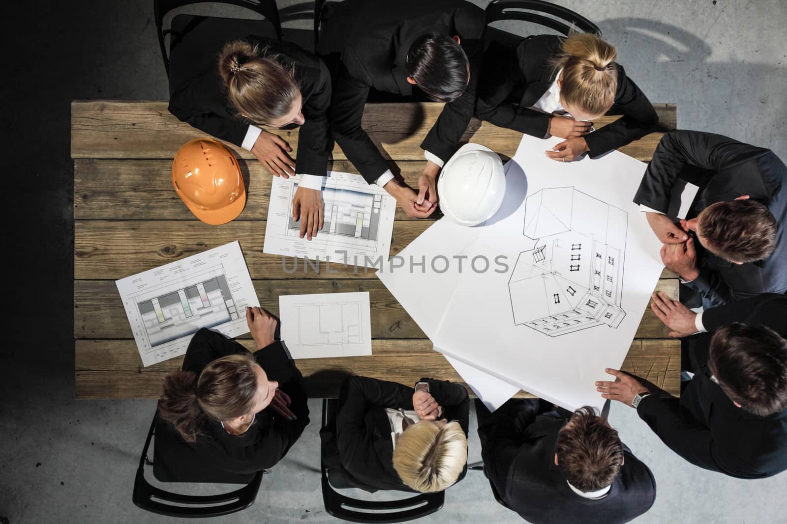 Business people discuss construction blueprint, hardhat on office table
