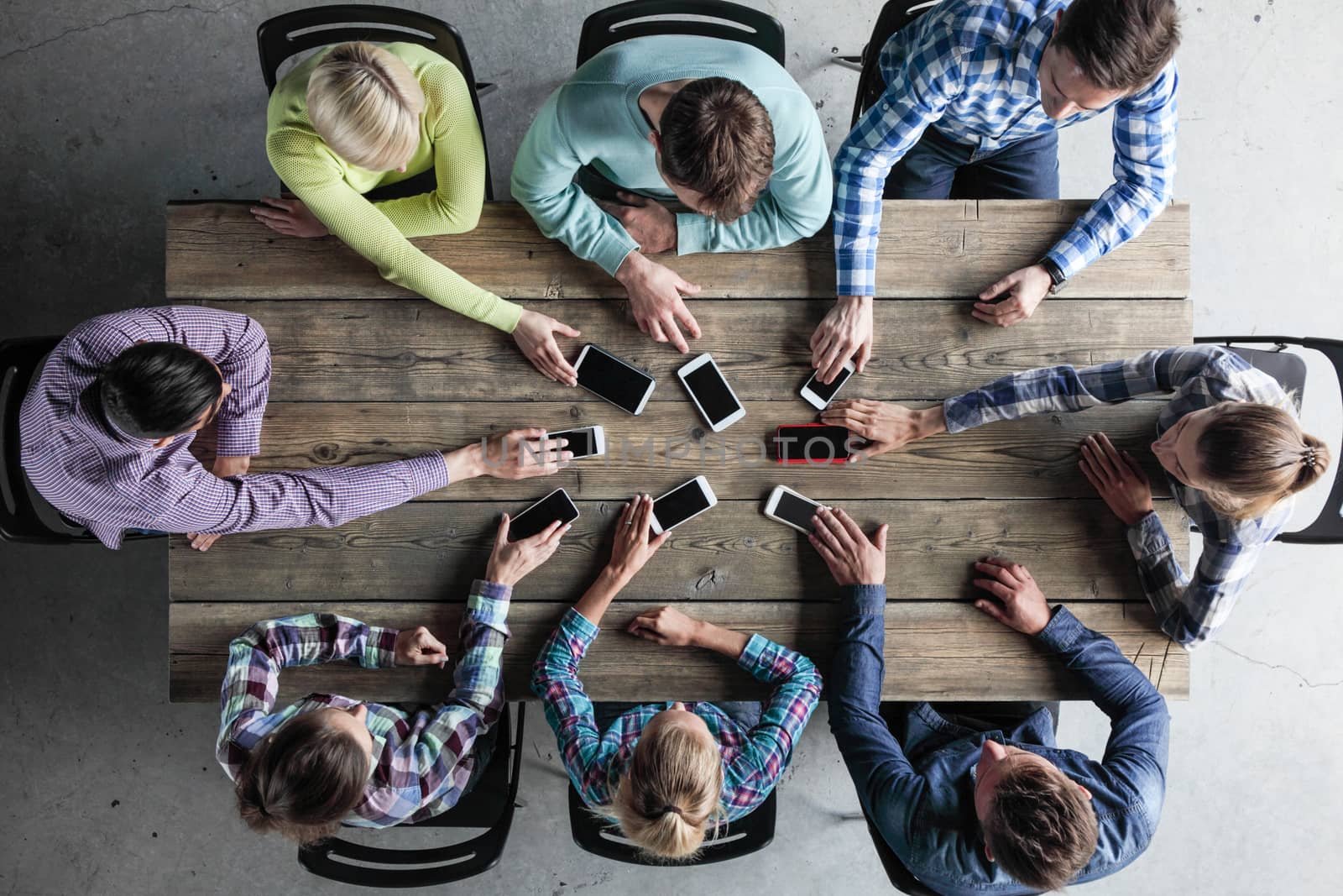 Team of business people in casual clothes sitting around the table, taking their mobile phones, top view