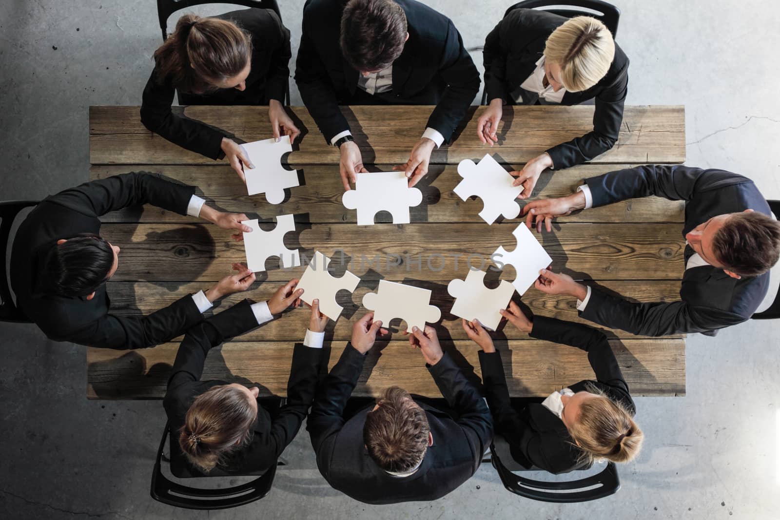 Business people and puzzle on wooden table, teamwork concept