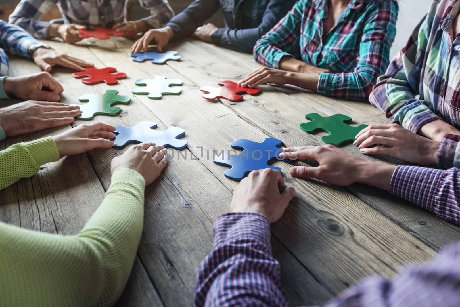 Business people and puzzle on wooden table, teamwork concept