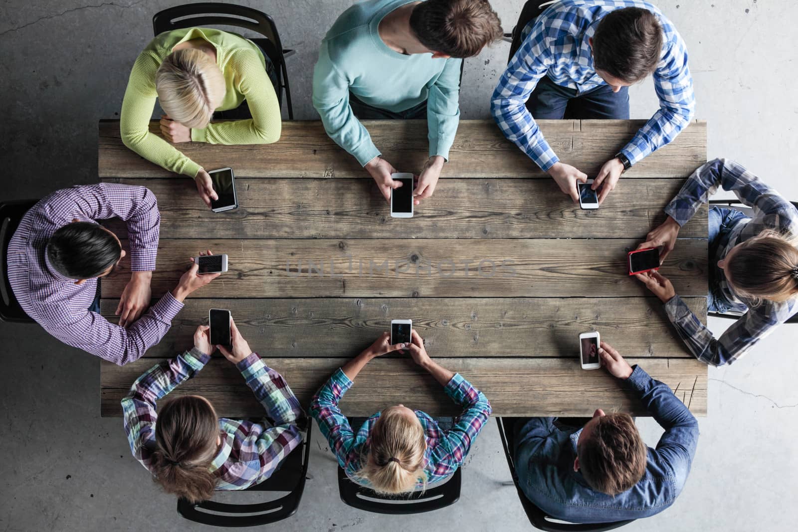 Team of business people in casual clothes sitting around the table, with their mobile phones, top view