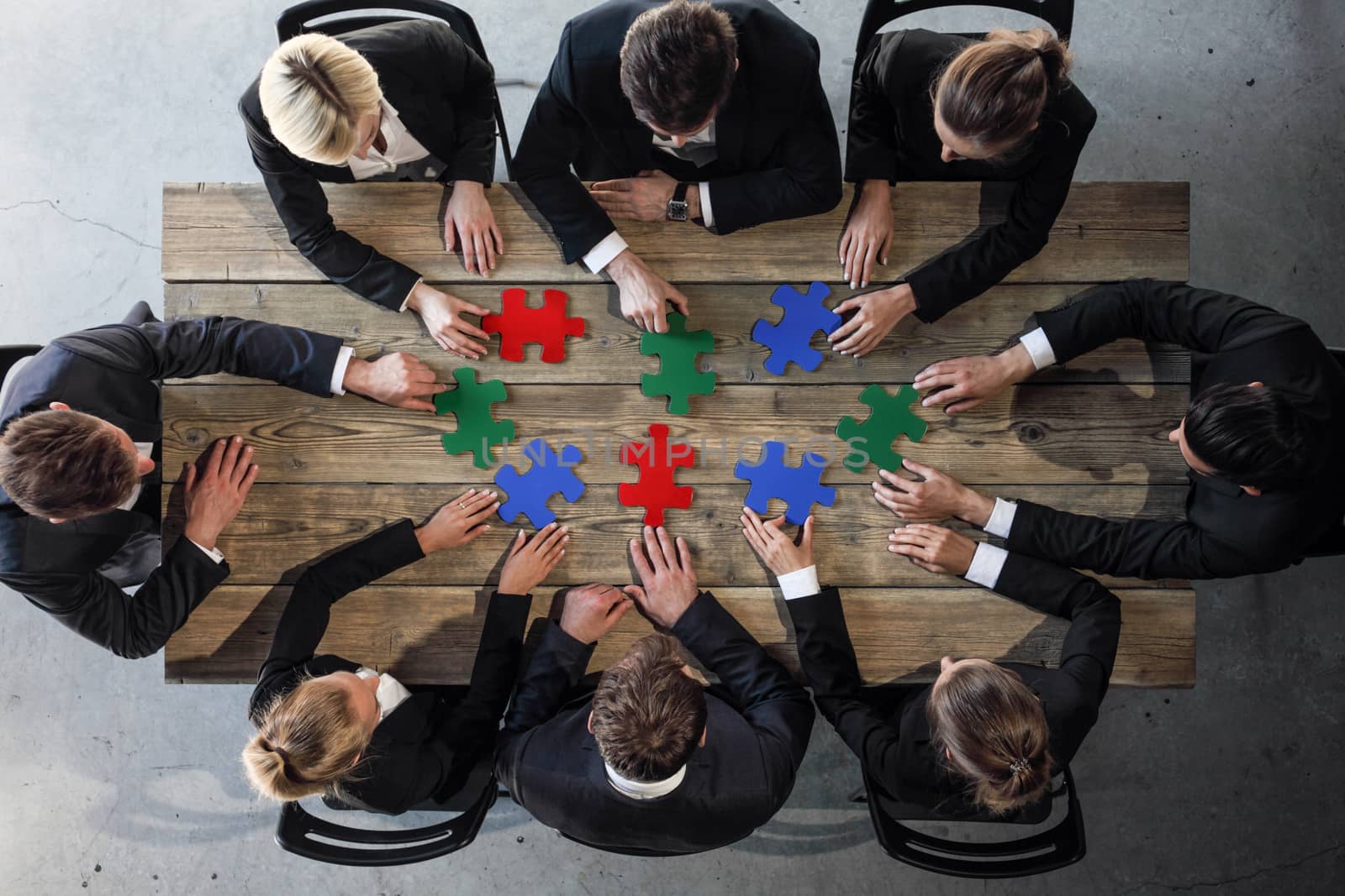 Business people and puzzle on wooden table, teamwork concept