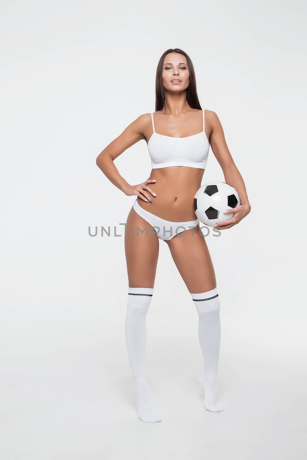 Female brunette in blanche lingerie and stockings staying with soccer ball and looking at camera