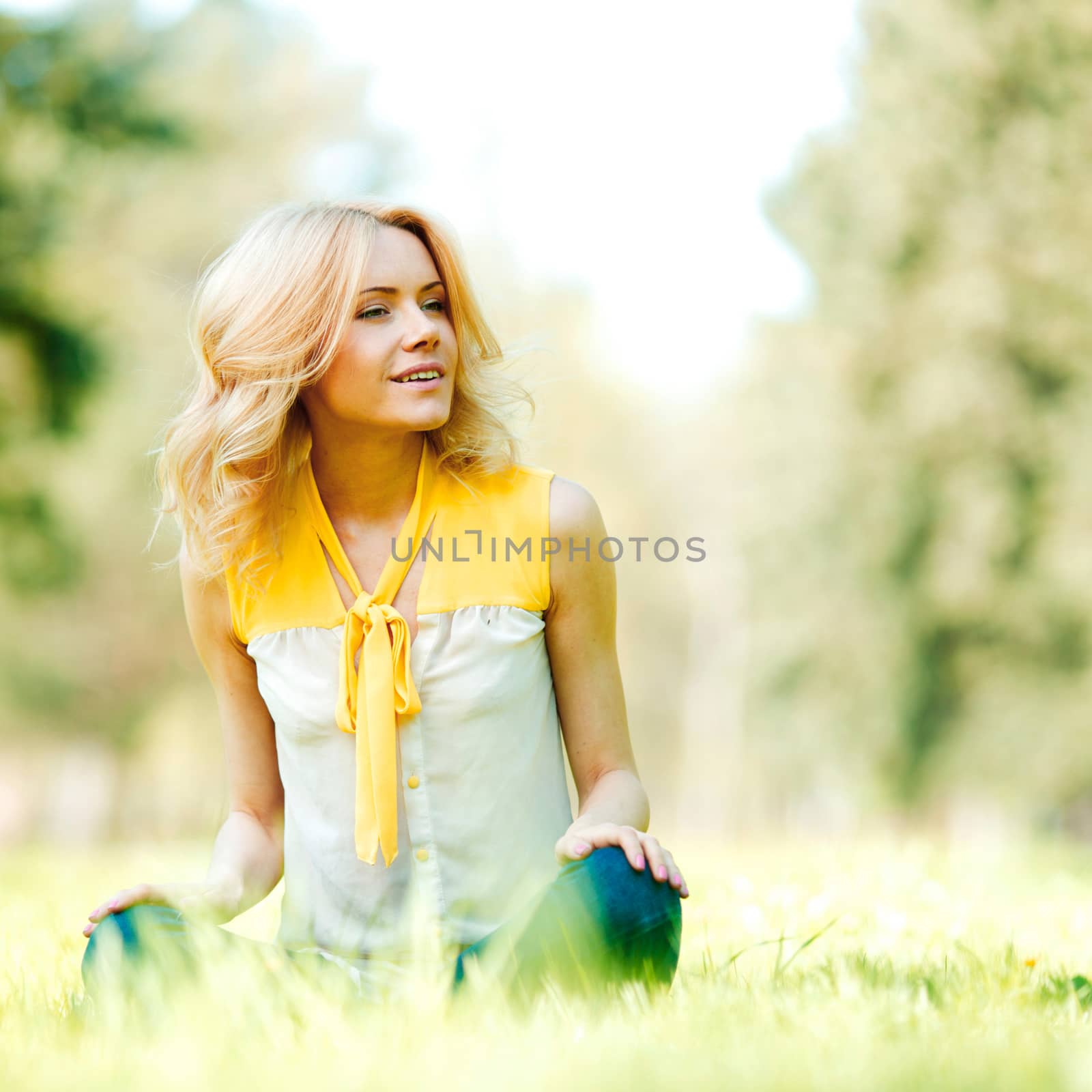 Beautiful young blond woman sitting on grass in park