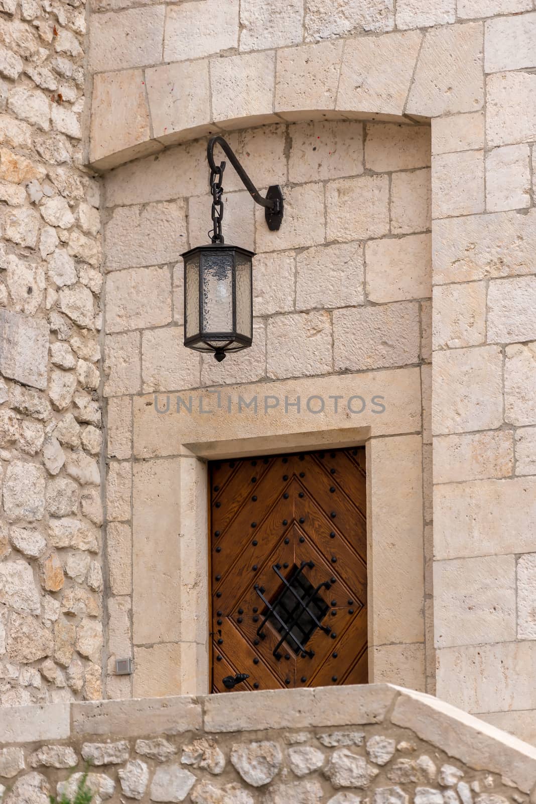 stone wall of a medieval building with a wooden door and a lantern above the entrance of a close-up