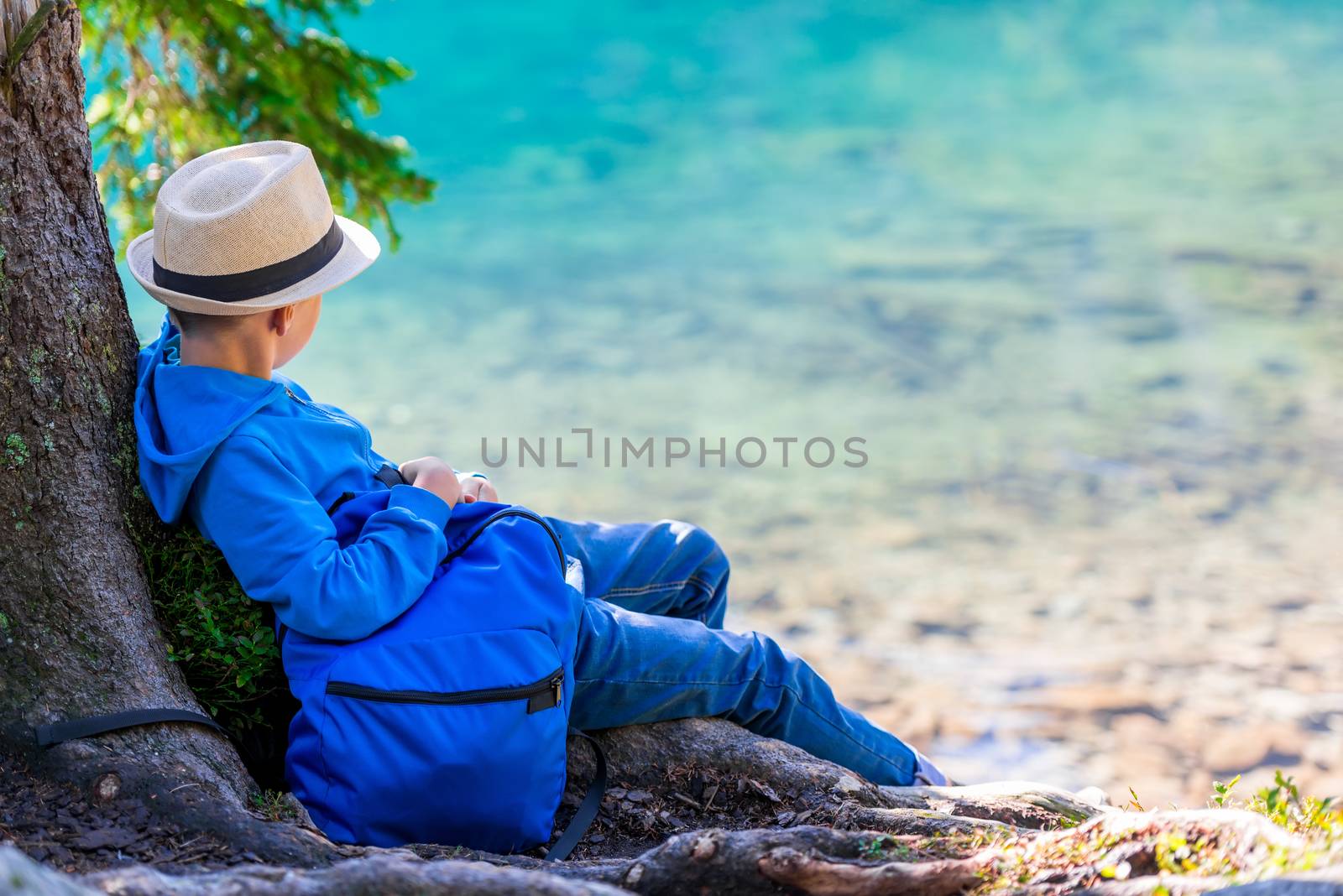 A boy of 8 years with a backpack resting by the lake in the Tatras