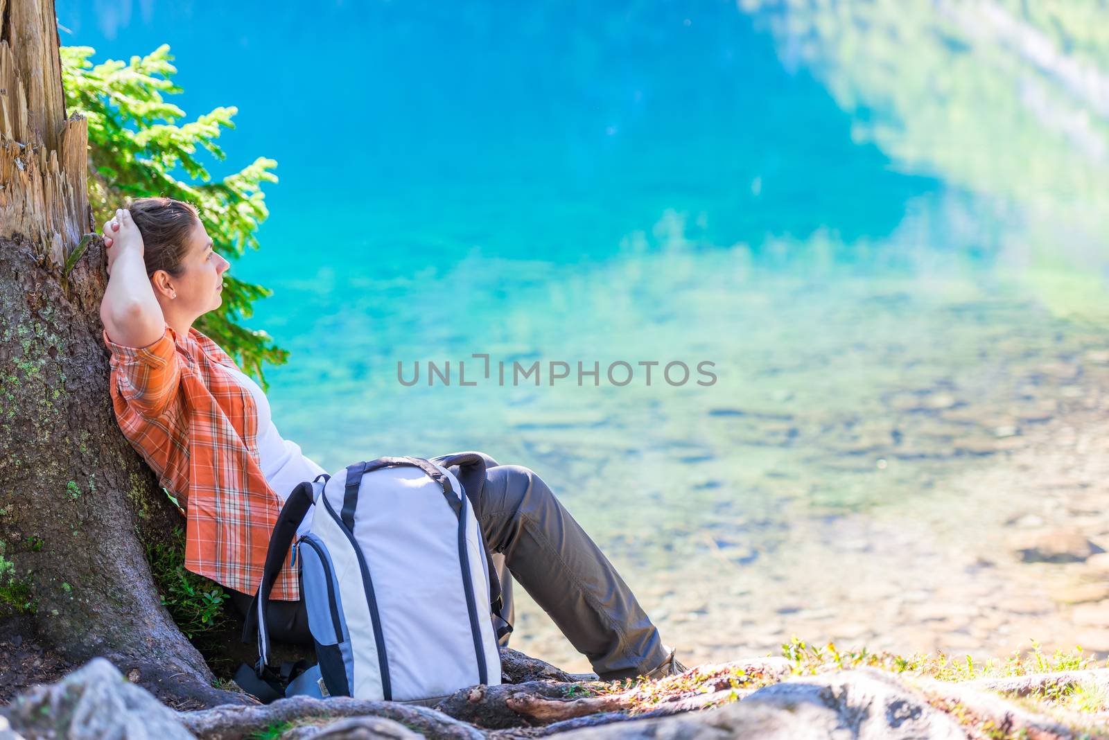 a relaxing traveler with a backpack sits at the Sea Eye in the Tatra mountains and admires