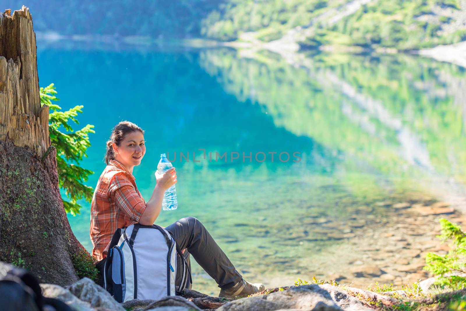 woman with a bottle of drinking water rests near a beautiful scenic lake in the mountains