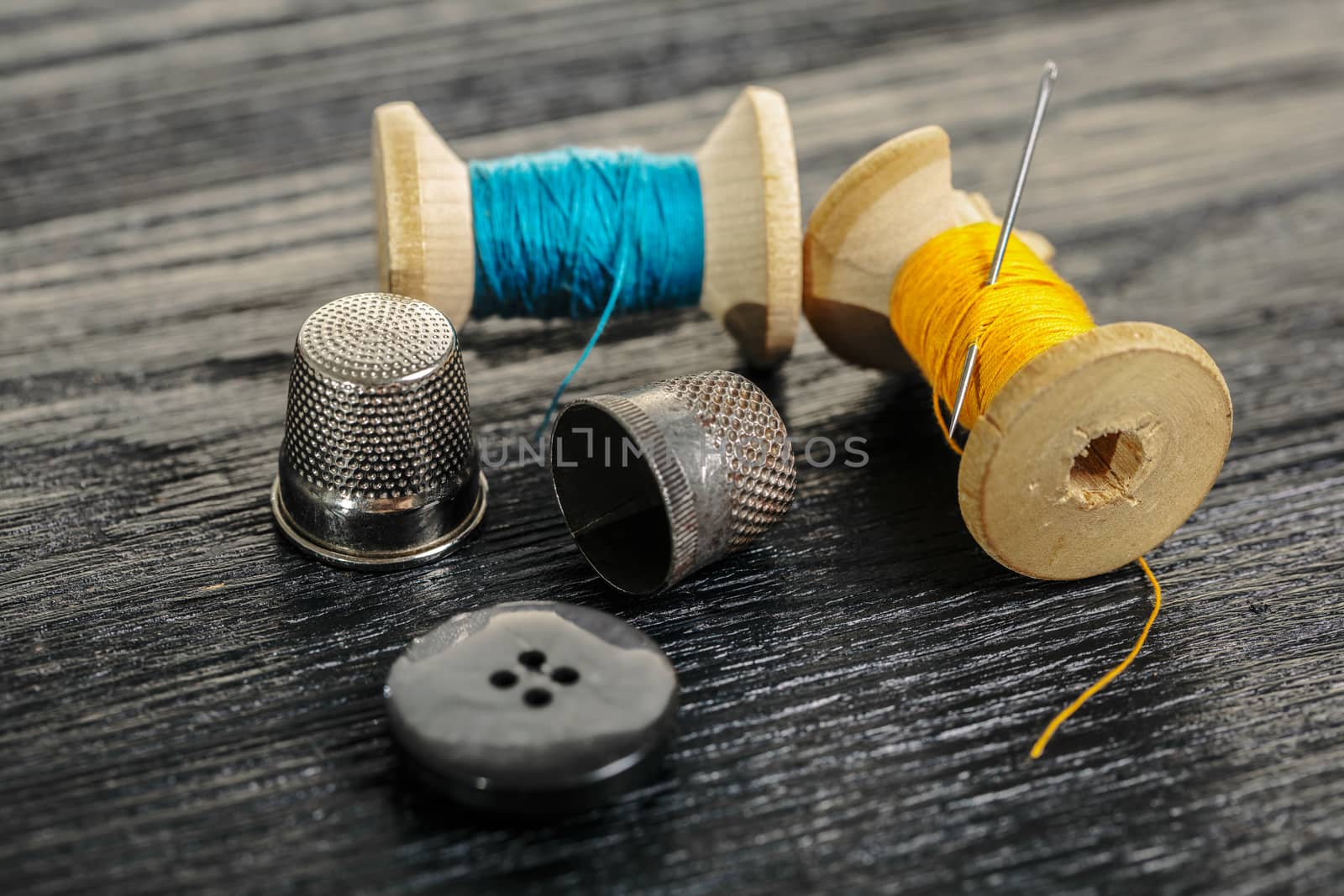 Thread with a thimble and button on black wooden background