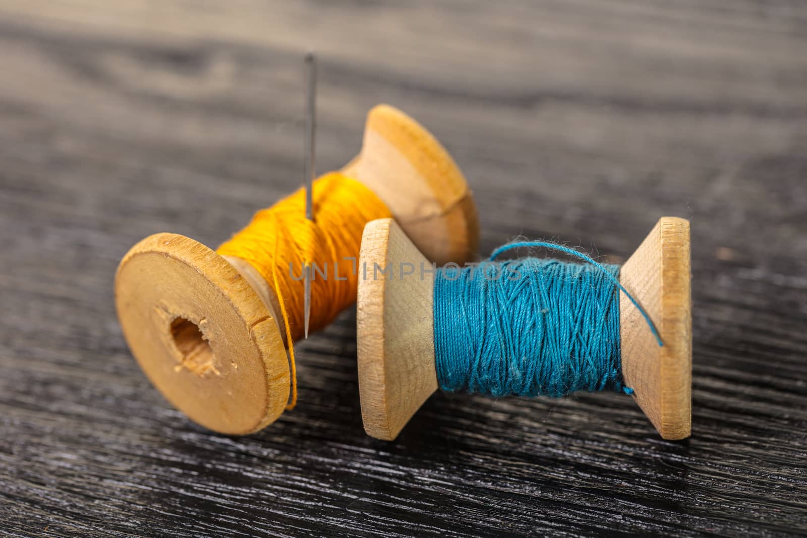 colored threads and needle on a black wooden background