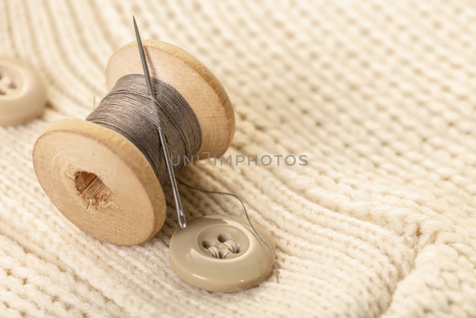 spool of thread with a needle on white knitted clothes