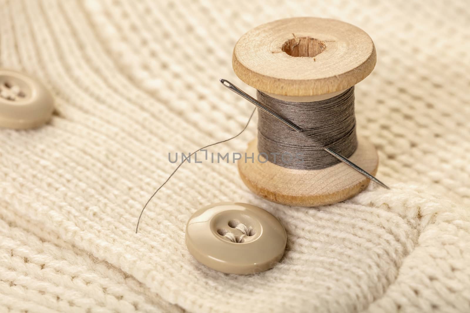 spool of thread with a needle on white knitted clothes