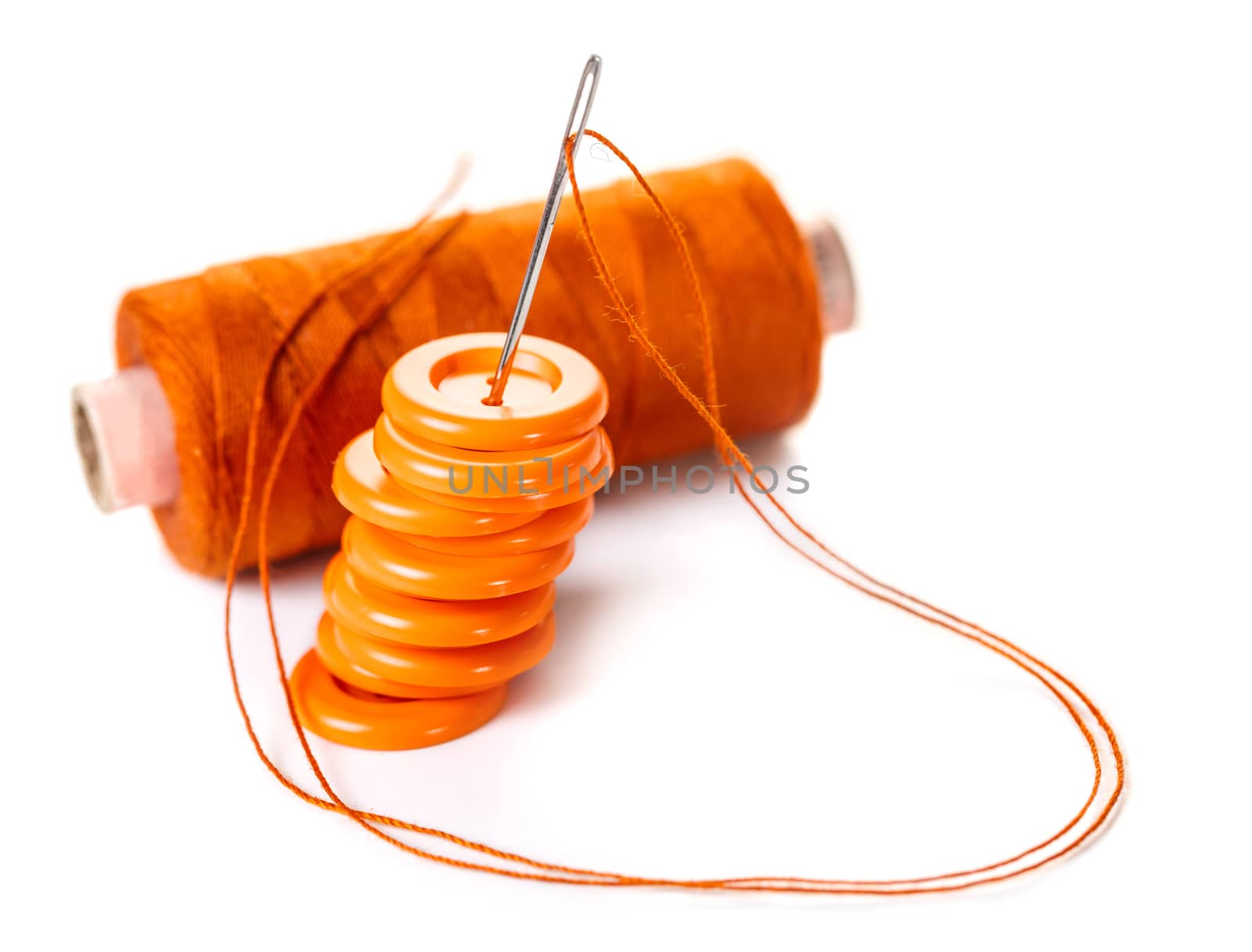 Needle with orange thread and buttons on a white background