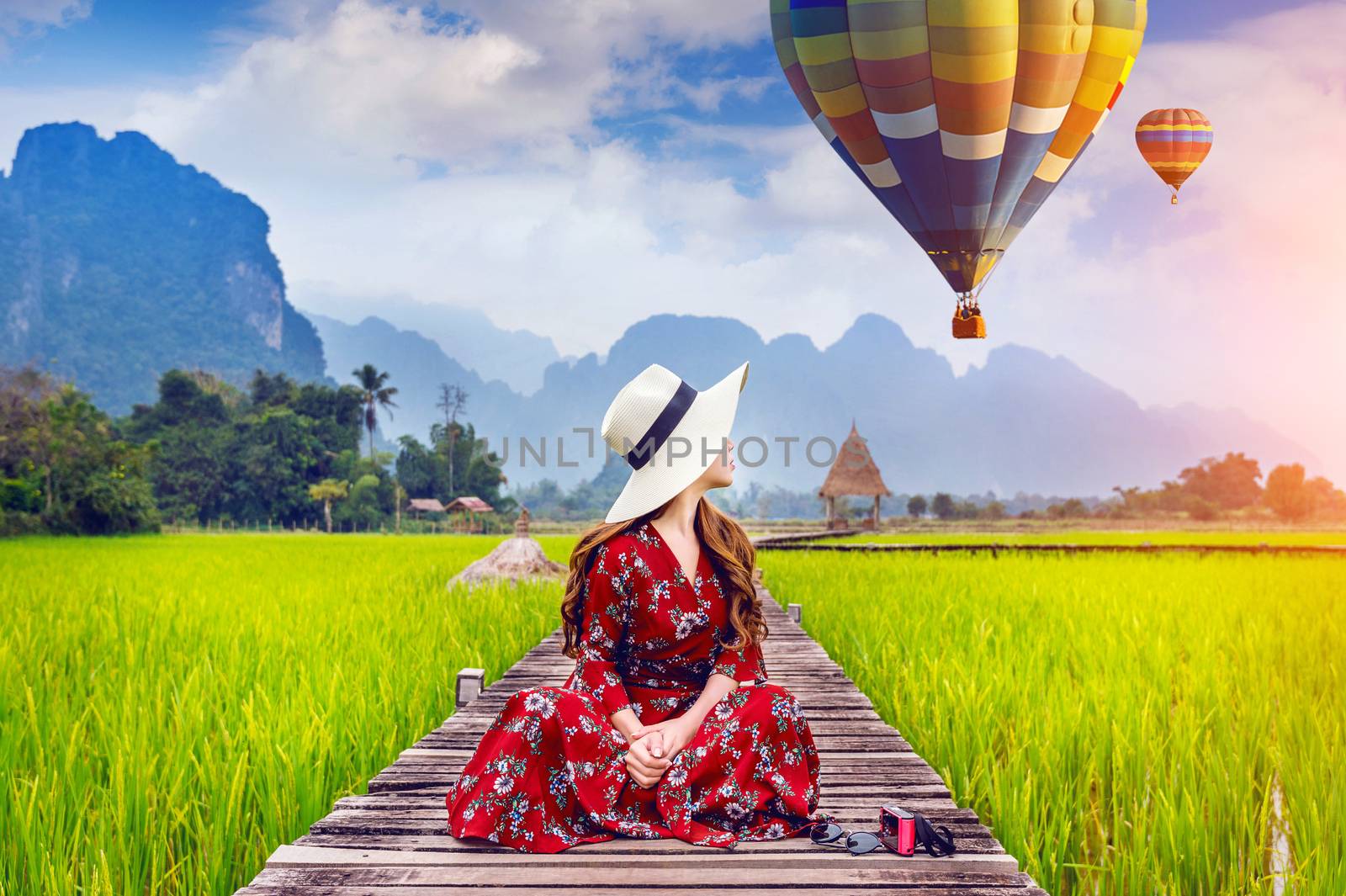 Young woman sitting on wooden path and look at balloons with green rice field in Vang Vieng, Laos. by gutarphotoghaphy