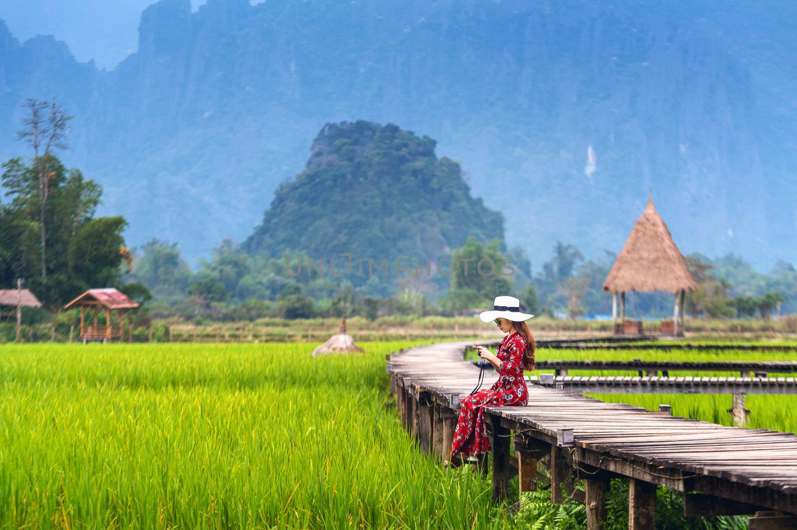 Young woman sitting on wooden path with green rice field in Vang Vieng, Laos. by gutarphotoghaphy