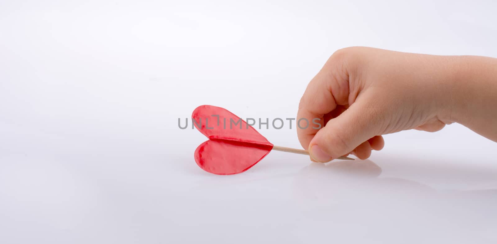 Little red color heart shape at the top of a stick in hand