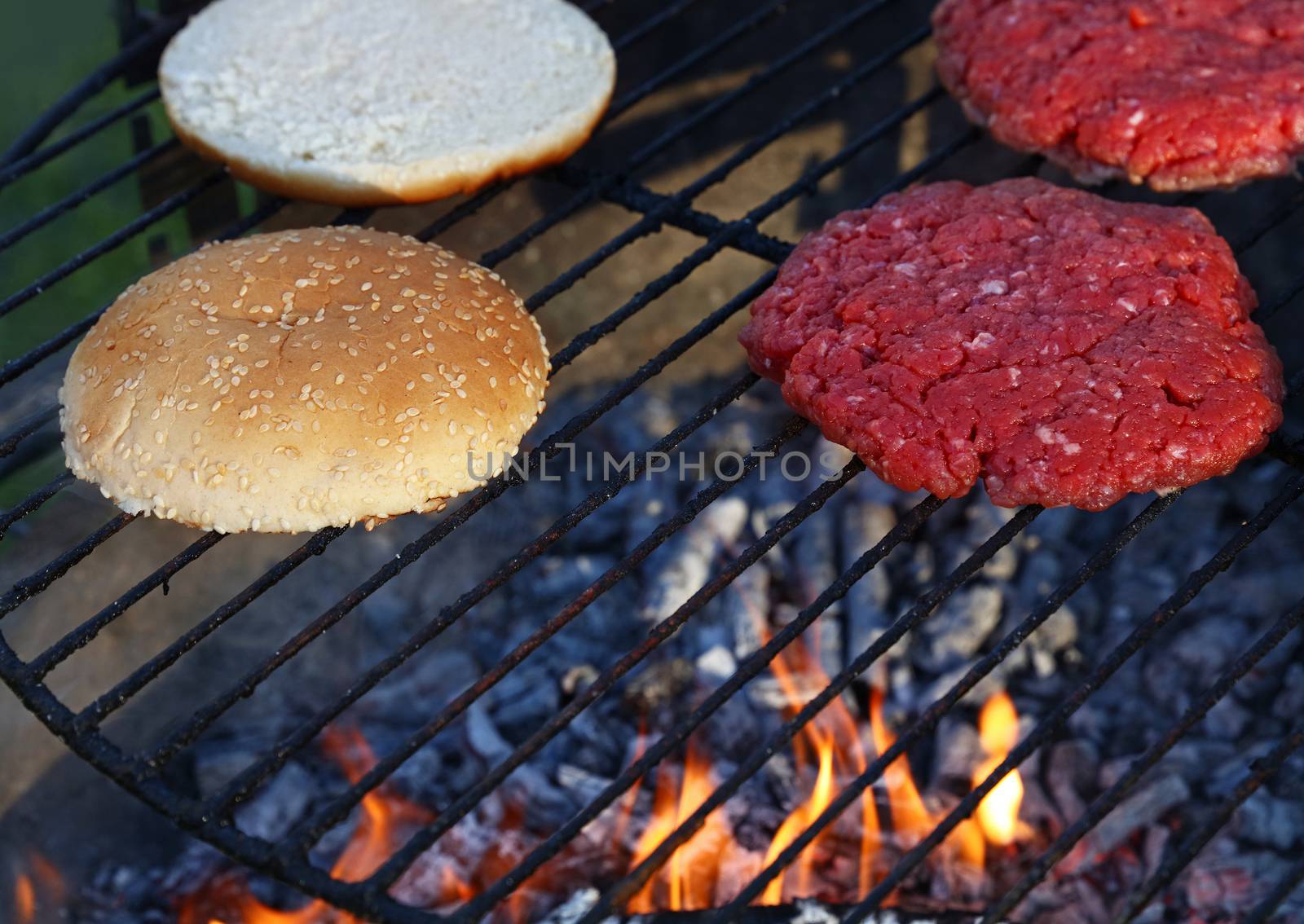 Meat burgers and buns for hamburger on fire grill by BreakingTheWalls