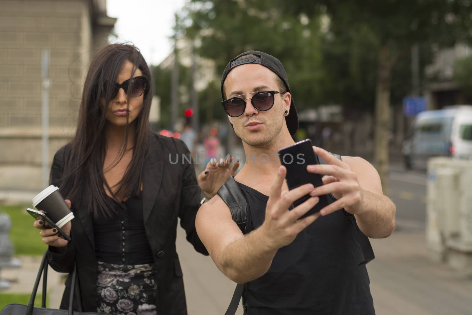 Young cheerful friends taking photos of themselves on smart phone, urban city outdoor scene, selective focus