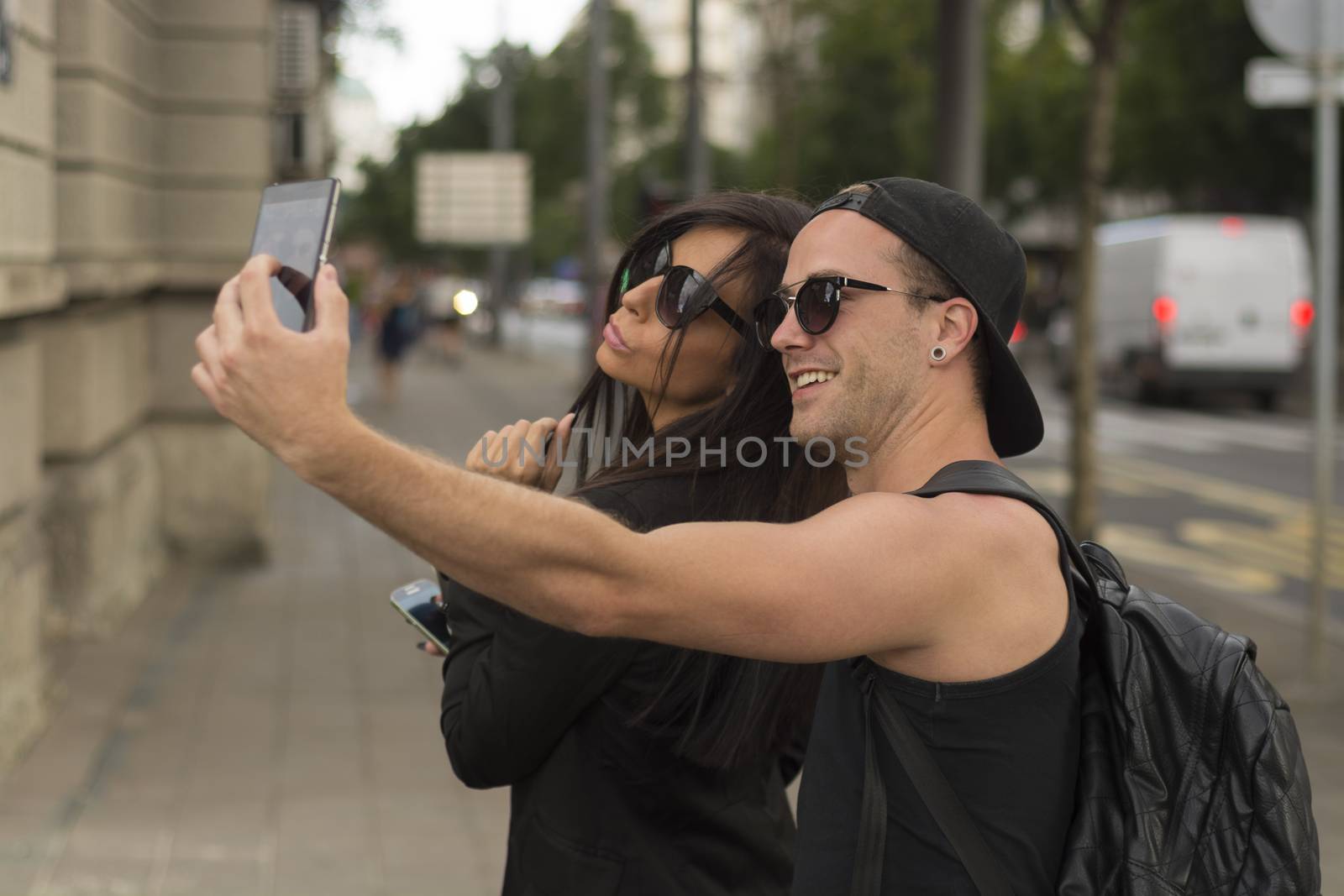 Young cheerful friends taking photos of themselves on smart phone, urban city outdoor scene, selective focus