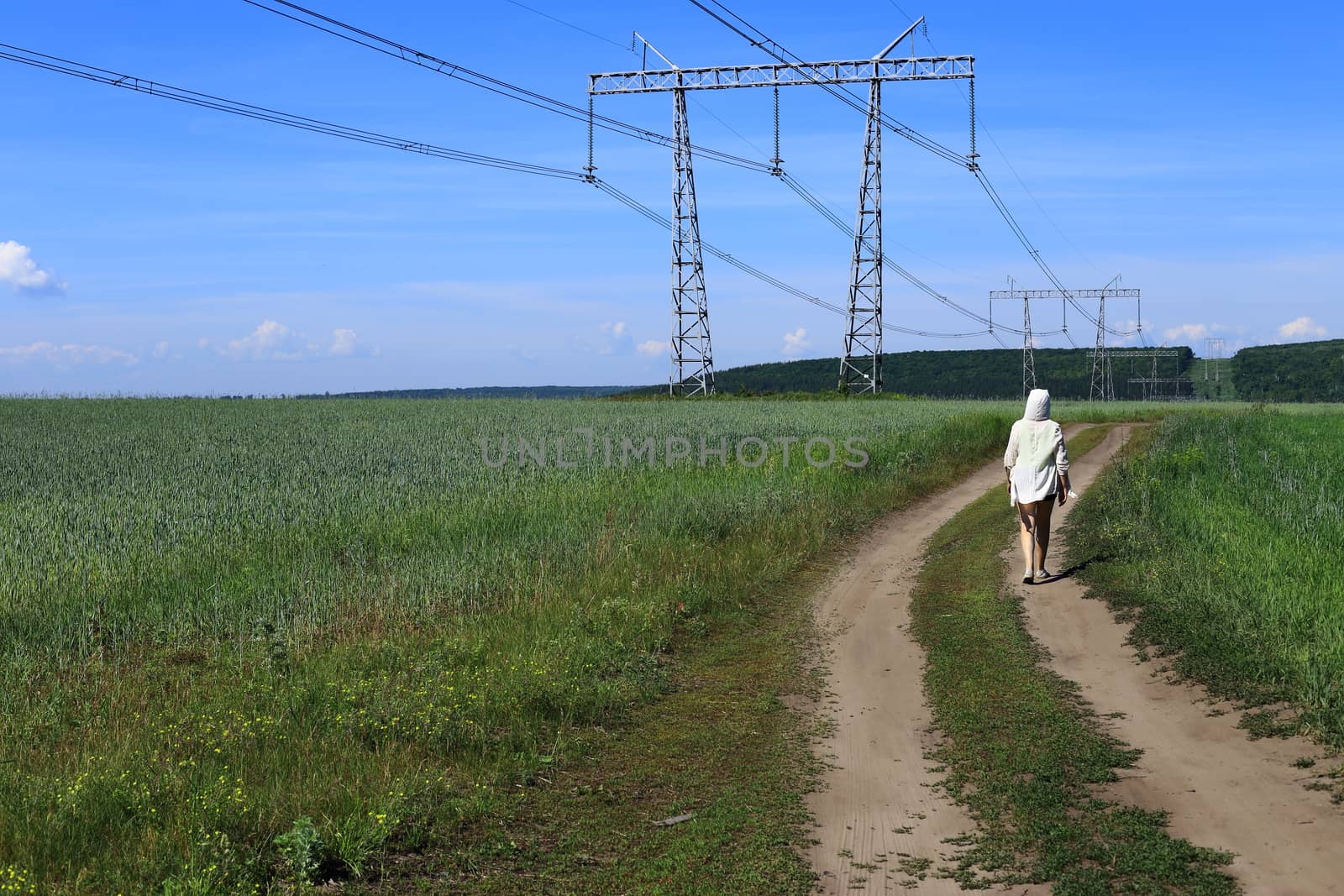 woman in a white sweater. view from the back. goes on the road. summer and green grass.