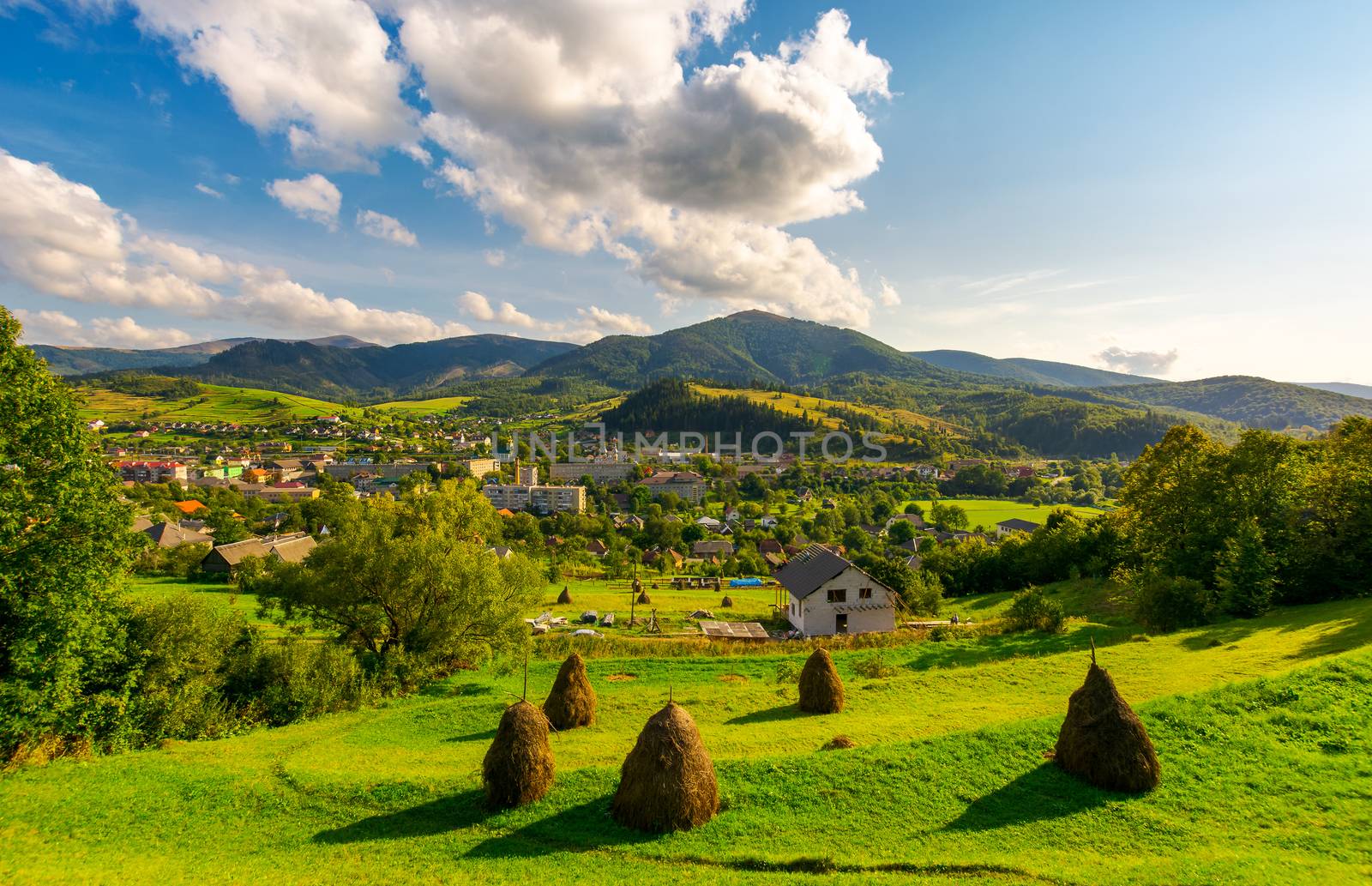 beautiful rural landscape in mountains. haystacks on the grassy hills. village at the foot of the mountain. interesting cloud formation over the ridge. lovely sunny afternoon