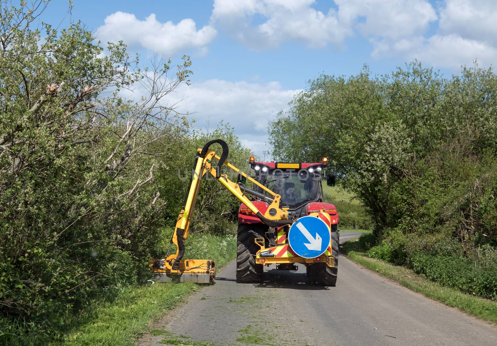 Grass verges being cut by large tractor mower in Sussex country lane during Springtime.