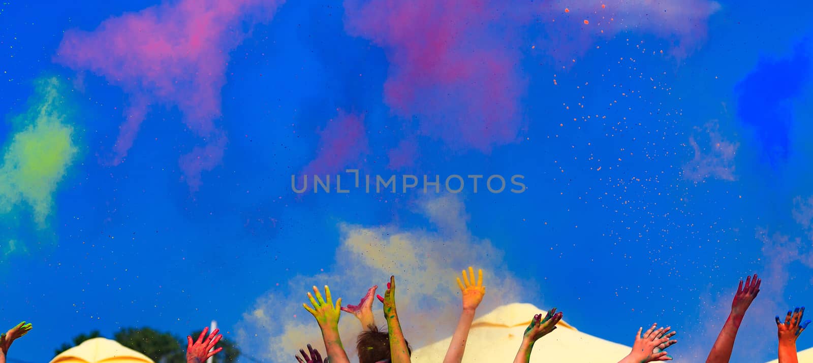 At the color Holi festival, hands in the air, blue sky behind