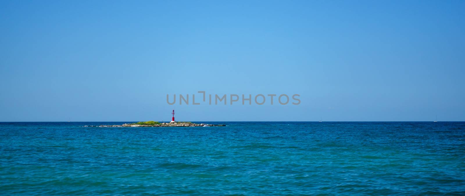 A small rocky island with a lighthouse, Adriatic sea, Mediterranean in Croatia, straight horizon line, clear blue sky