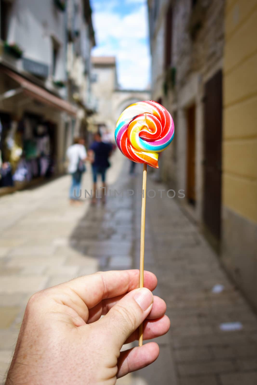 Hand holding colorful lolipop, old city street blurred as background