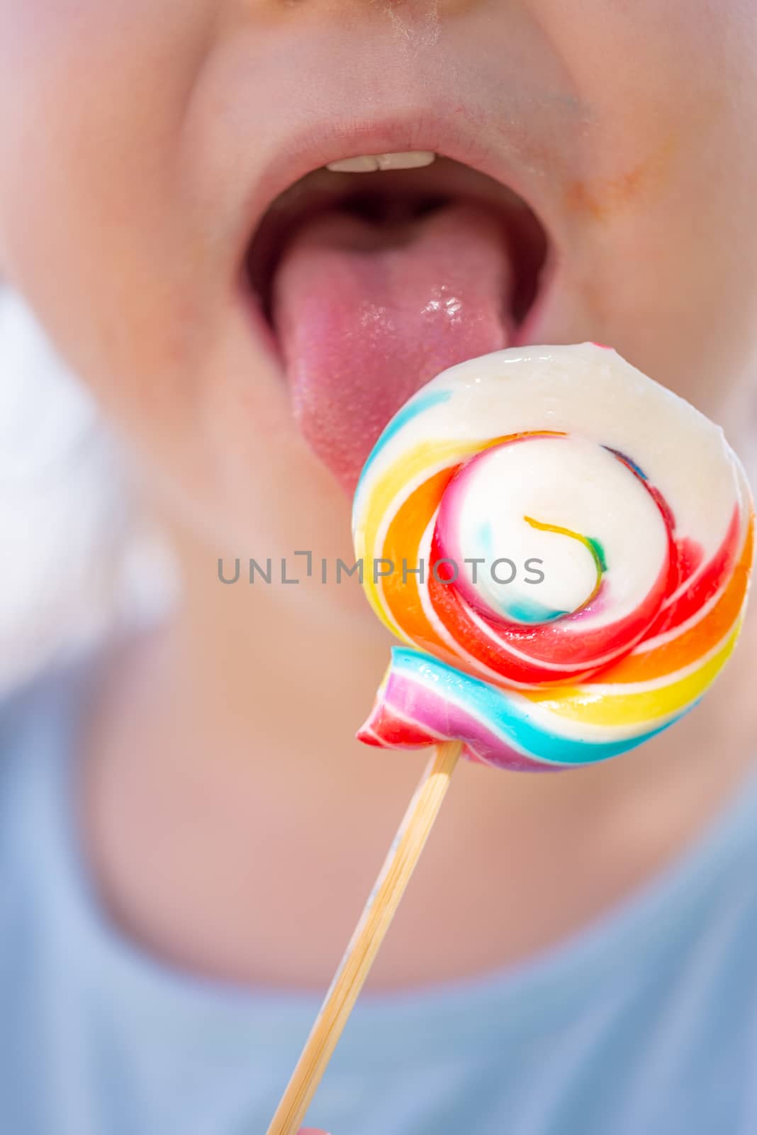 Little kid, child with colorful lolipop, licking on the lolipop, unrecognizable