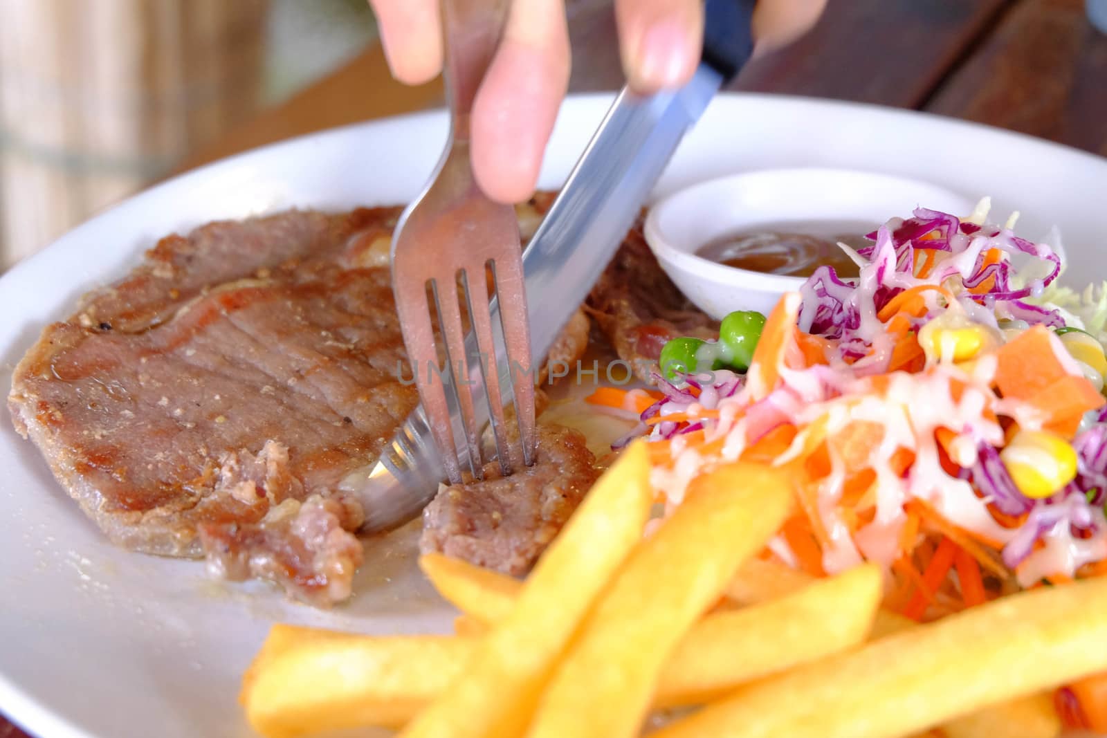 Close up of a cutting a fillet steak with french fries and vegetable salad