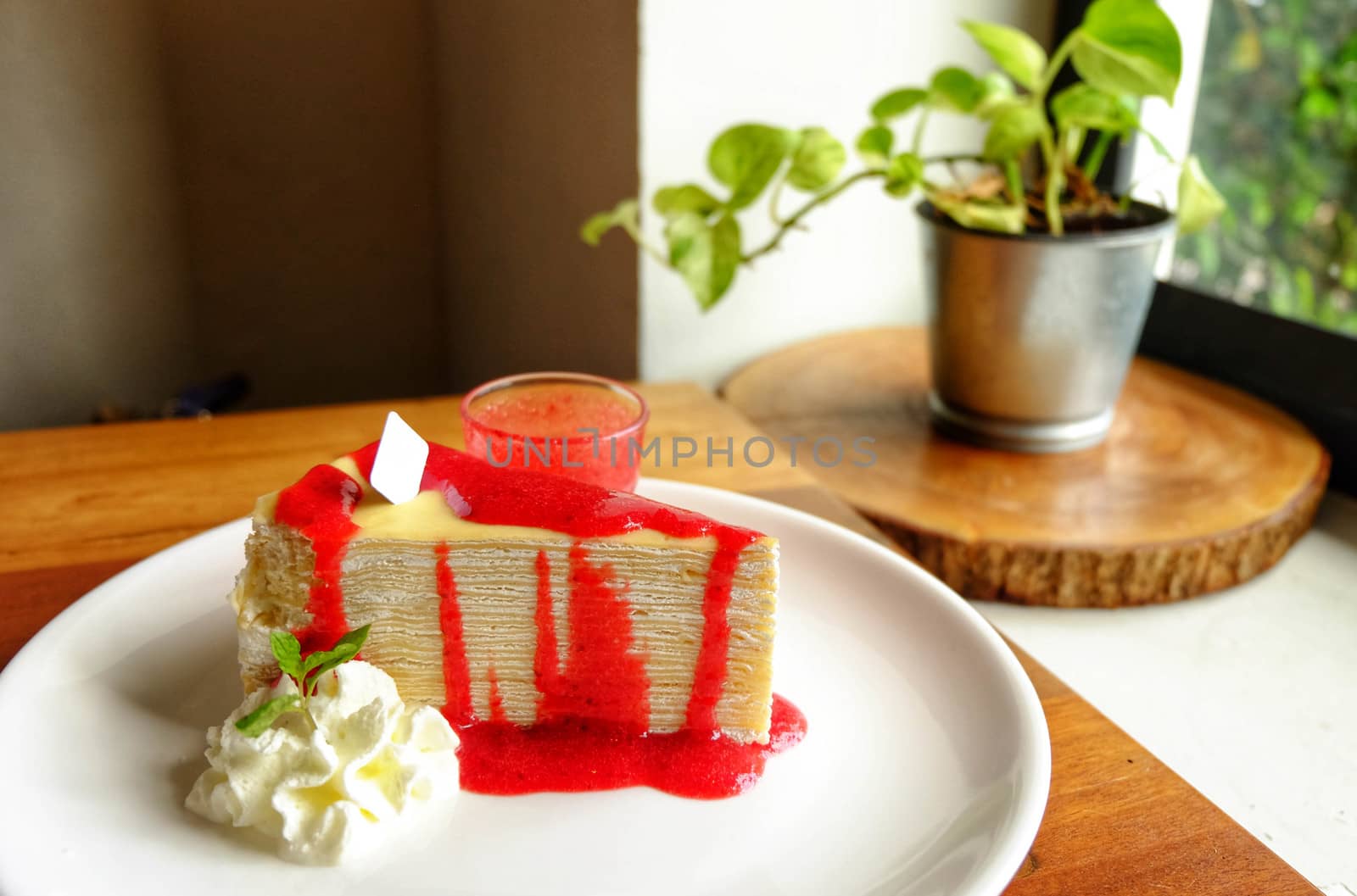 Crepe cake with cream and strawberry on top and sauce in ceramic by e22xua