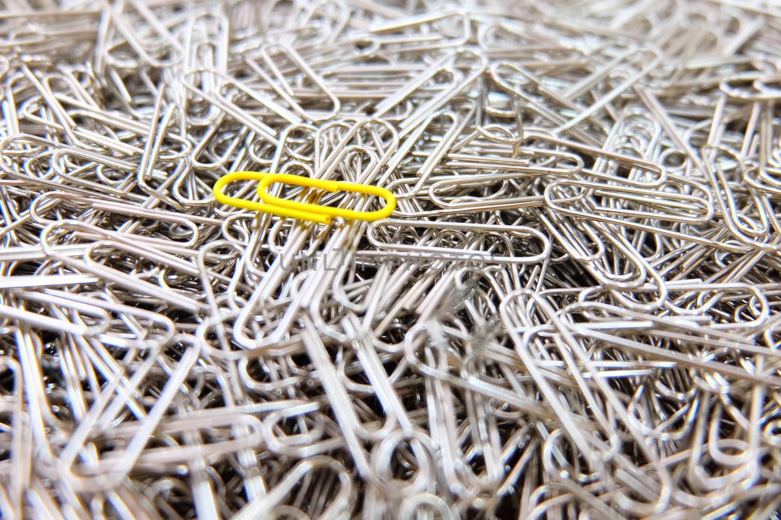 Yellow paper clip on multiple paper clips background. by e22xua