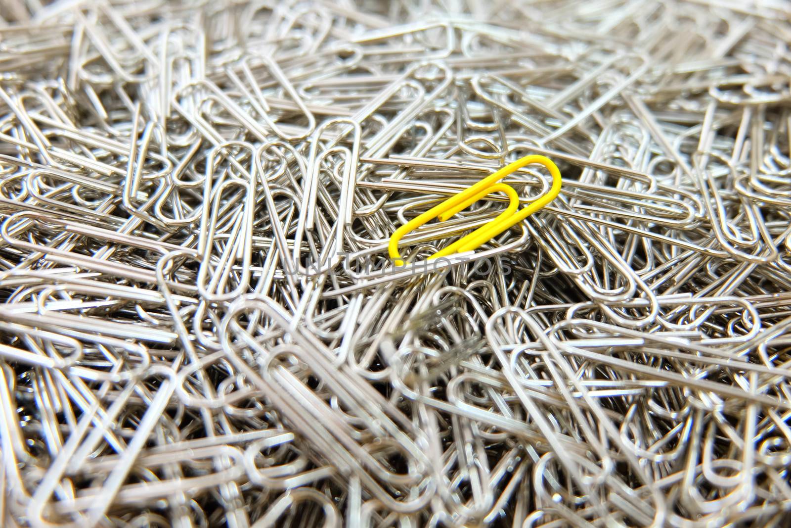 Yellow paper clip on multiple paper clips background. by e22xua