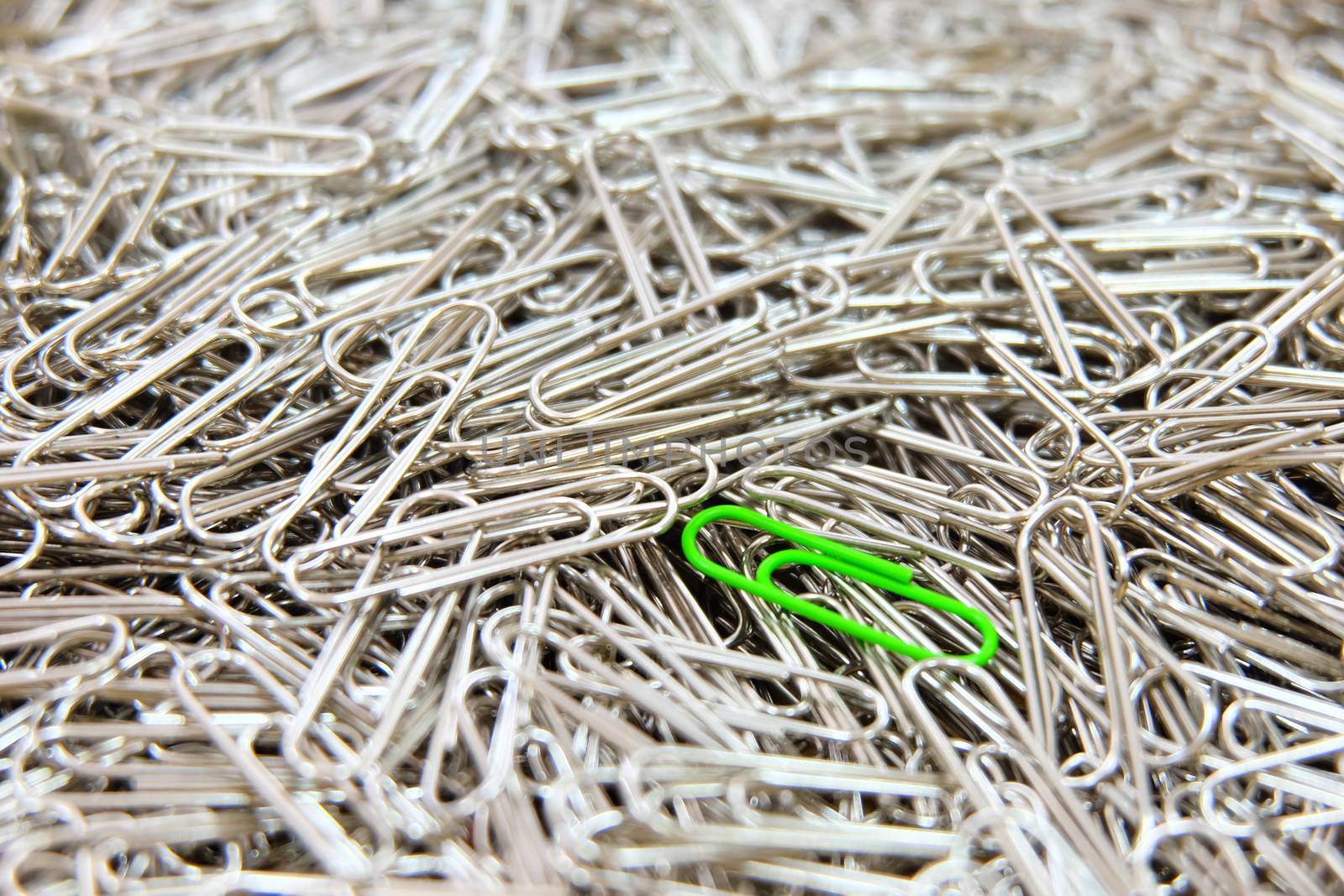 Green paper clip on multiple paper clips background.