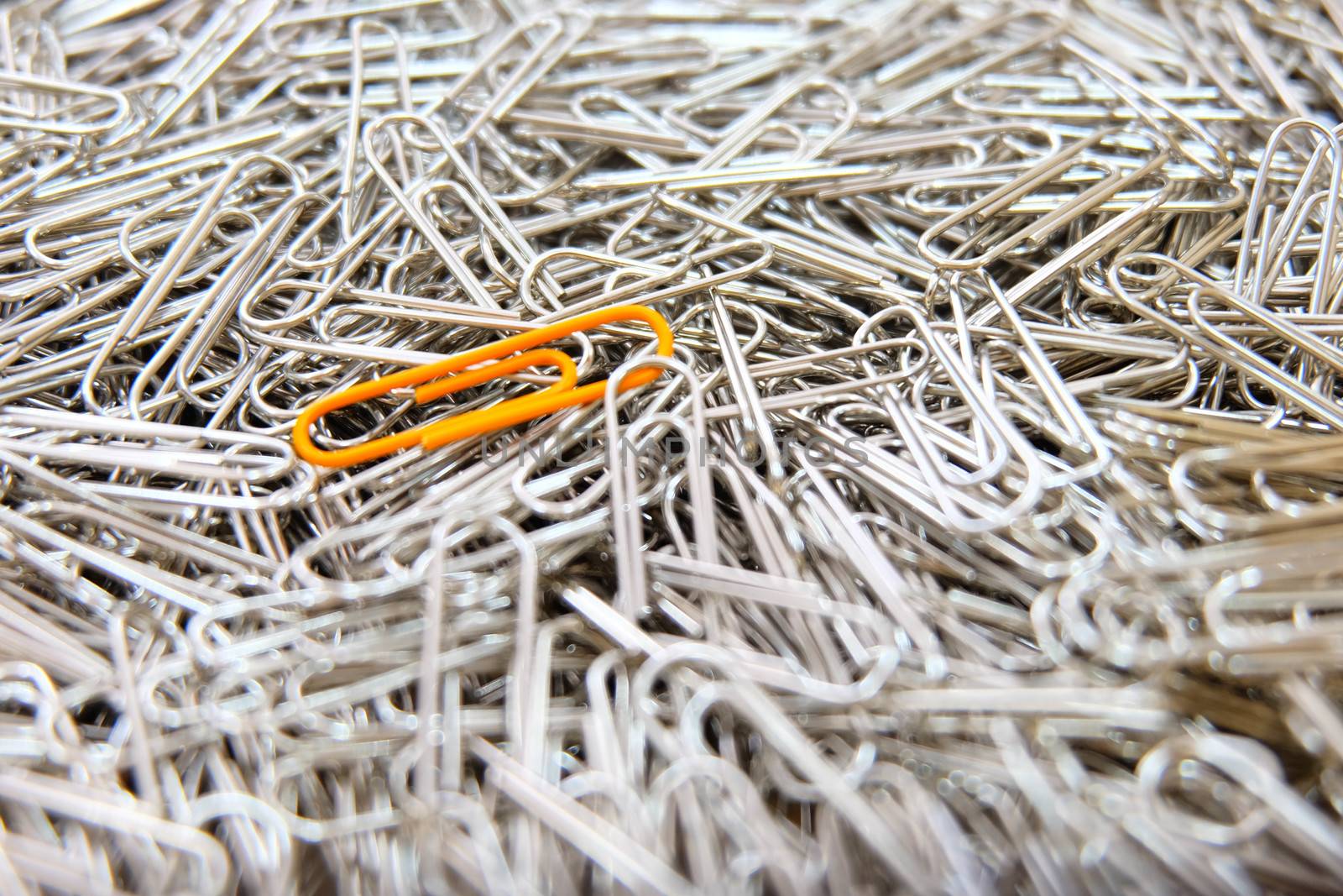 Orange paper clip on multiple paper clips background. by e22xua