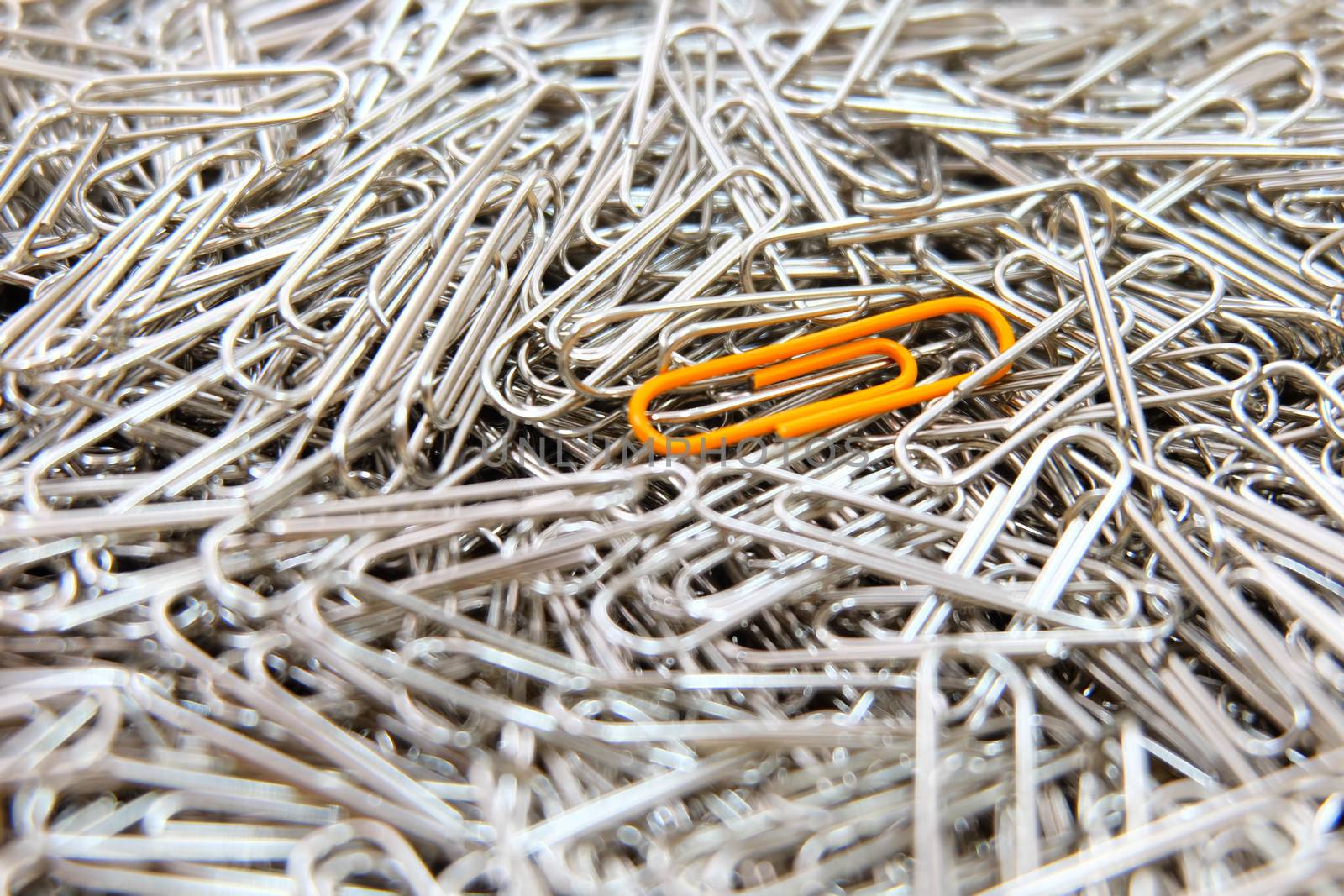 Orange paper clip on multiple paper clips background. by e22xua